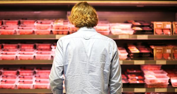 Junger Mann, steht im Supermarkt vor einem Fleischregal.