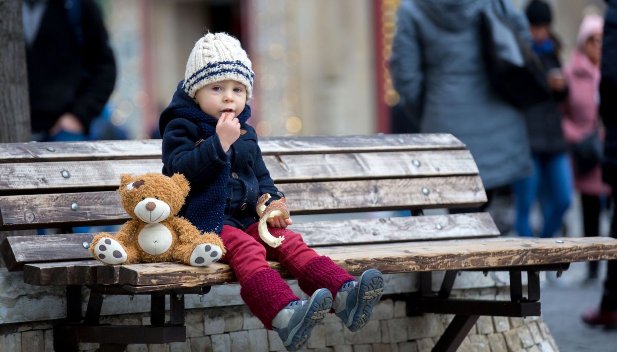 Kind sitzt in der Stadt auf einer Bank 