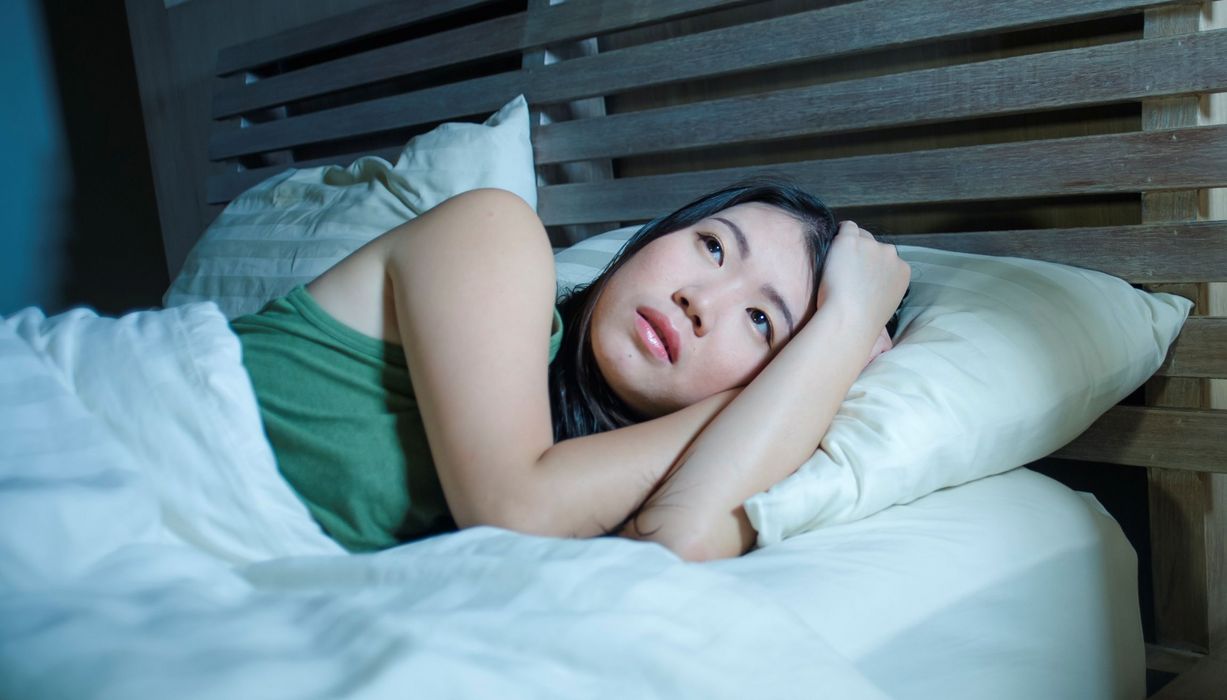 Frau liegt mit offenen Augen im Bett: Sie würde gerne schlafen, kann aber nicht.