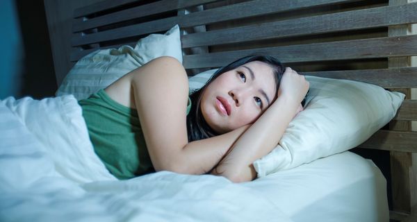 Frau liegt mit offenen Augen im Bett: Sie würde gerne schlafen, kann aber nicht.