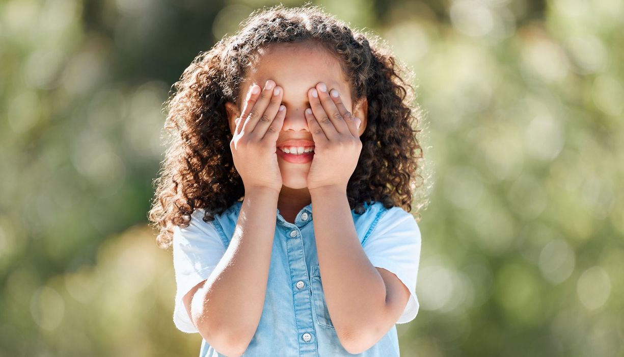Lächelndes Grundschulkind hält sich die Augen zu.