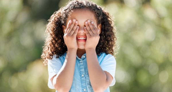Lächelndes Grundschulkind hält sich die Augen zu.