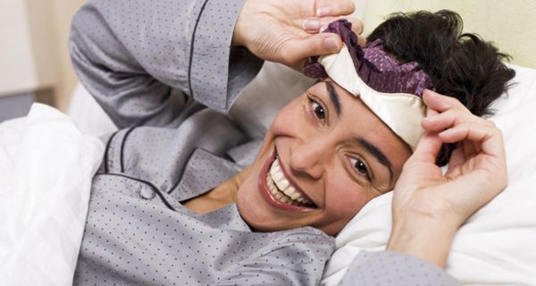 Frau liegt mit Schlafmaske im Bett.