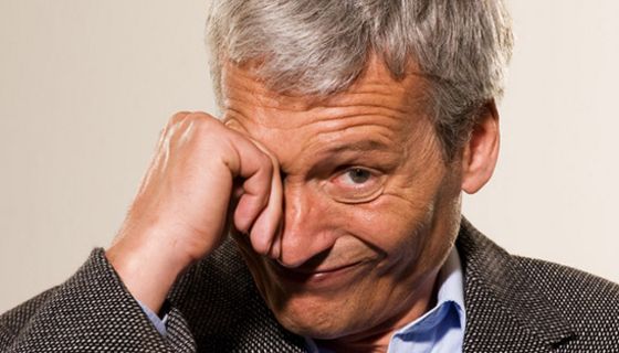 Porträt: Mann um die 60, Jacket, blaues Hemd, grauhaarig, reibt sich mit der rechten Hand das rechte Auge
