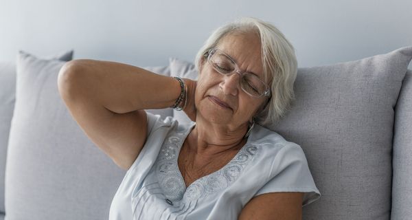 Ältere Frau mit verspanntem Nacken auf dem Sofa