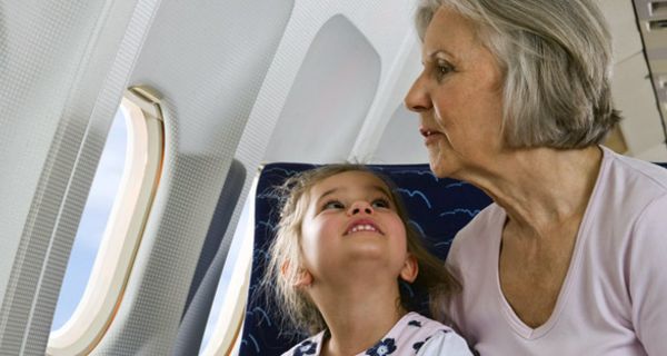 Ältere Frau und kleines Kind sitzen gemeinsam im Flugzeug und schauen nach draußen.