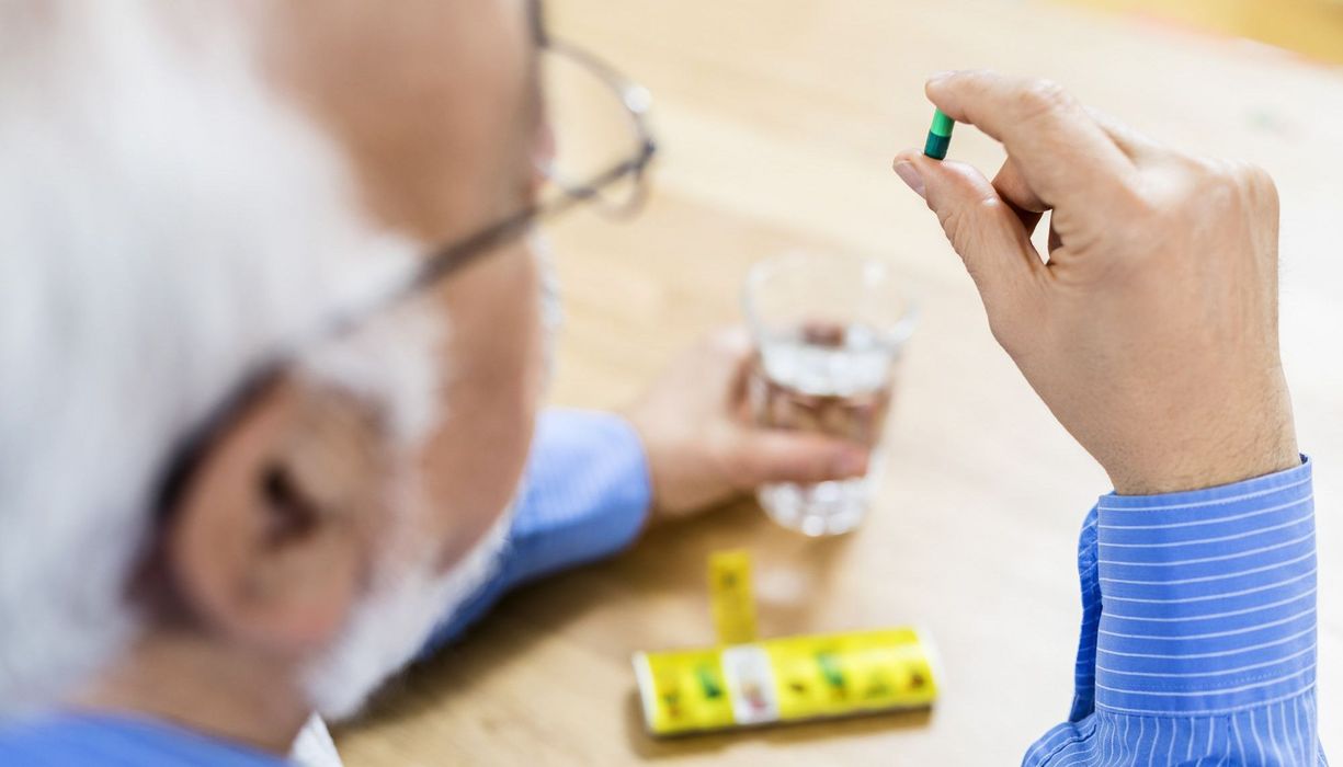 Älterer Mann mit Pillendose und einer Tablette in der Hand.