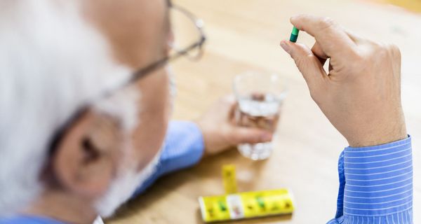 Älterer Mann mit Pillendose und einer Tablette in der Hand.