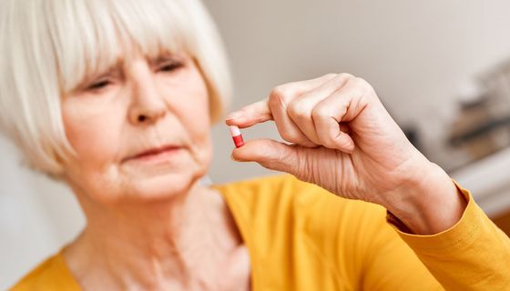 Frau, hält eine Pille in der Hand und betrachtet sie.