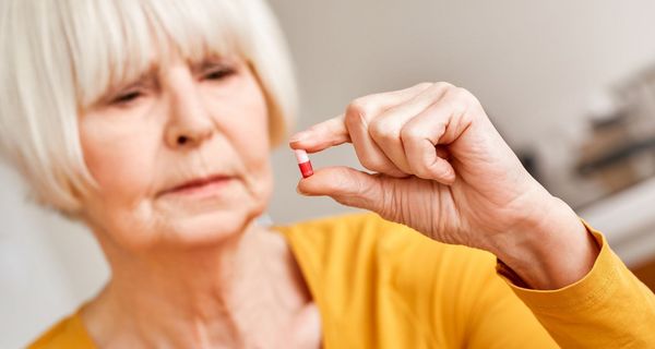 Frau, hält eine Pille in der Hand und betrachtet sie.