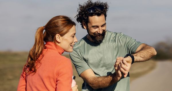 Ein Paar in Sportkleidung blickt auf die Smartwatch an seinem Handgelenk, beide scheinen sich darüber zu freuen.