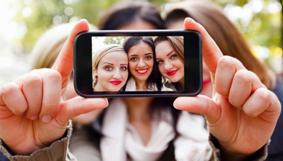 Drei Teenager-Mädchen stecken die Köpfe zusammen und machen ein Handyfoto von sich