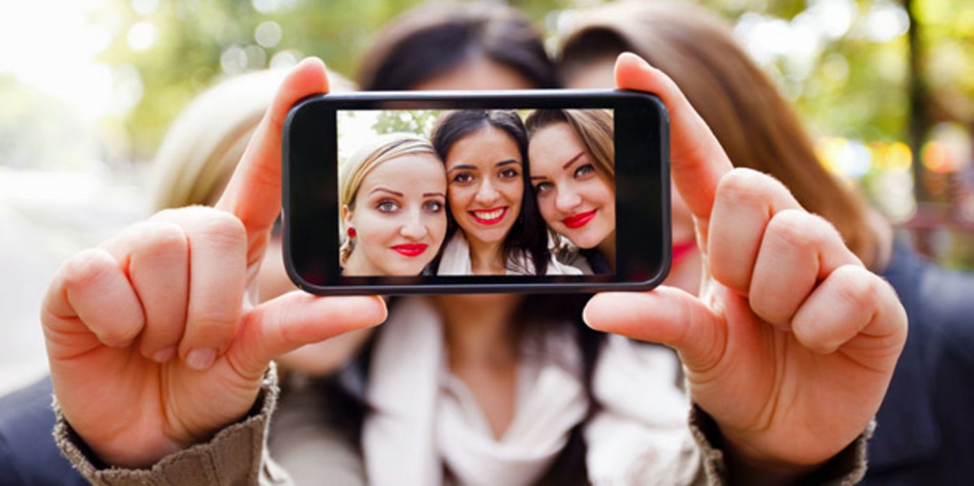 Drei Teenager-Mädchen stecken die Köpfe zusammen und machen ein Handyfoto von sich