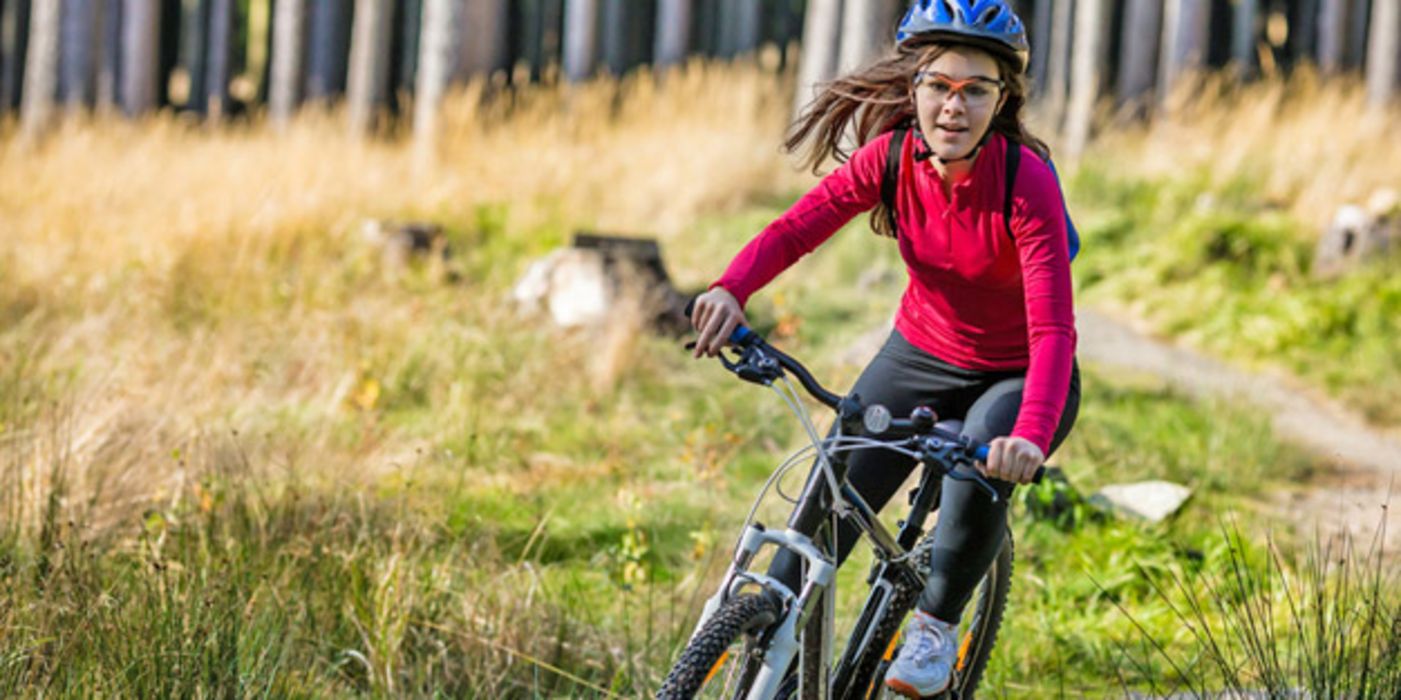 Mädchen, ca. 11 Jahre, auf Mountainbike fährt auf Waldweg, wehende Haare, rotes Shirt, blauer Helm