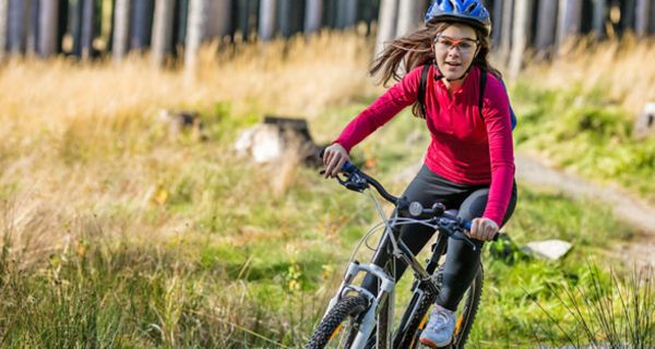 Mädchen, ca. 11 Jahre, auf Mountainbike fährt auf Waldweg, wehende Haare, rotes Shirt, blauer Helm