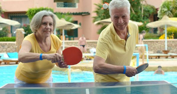 Frontalfoto: Älteres Paar beim Tischtennisspielen auf einer Seite der Platte, Kamera zugewandt