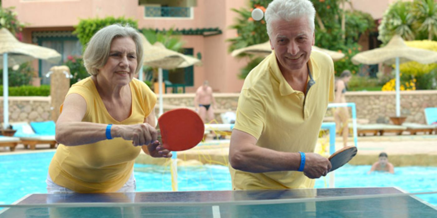 Frontalfoto: Älteres Paar beim Tischtennisspielen auf einer Seite der Platte, Kamera zugewandt