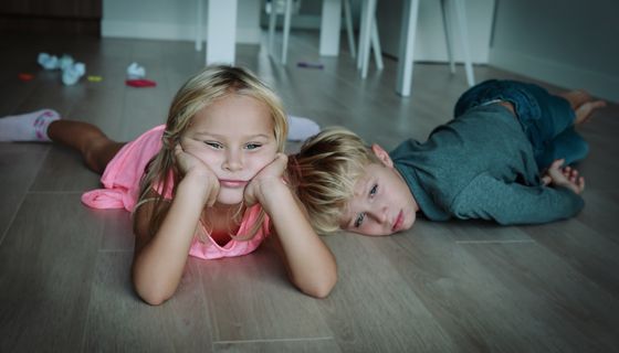 Zwei Kinder, liegen gelangweilt und deprimiert auf dem Boden.