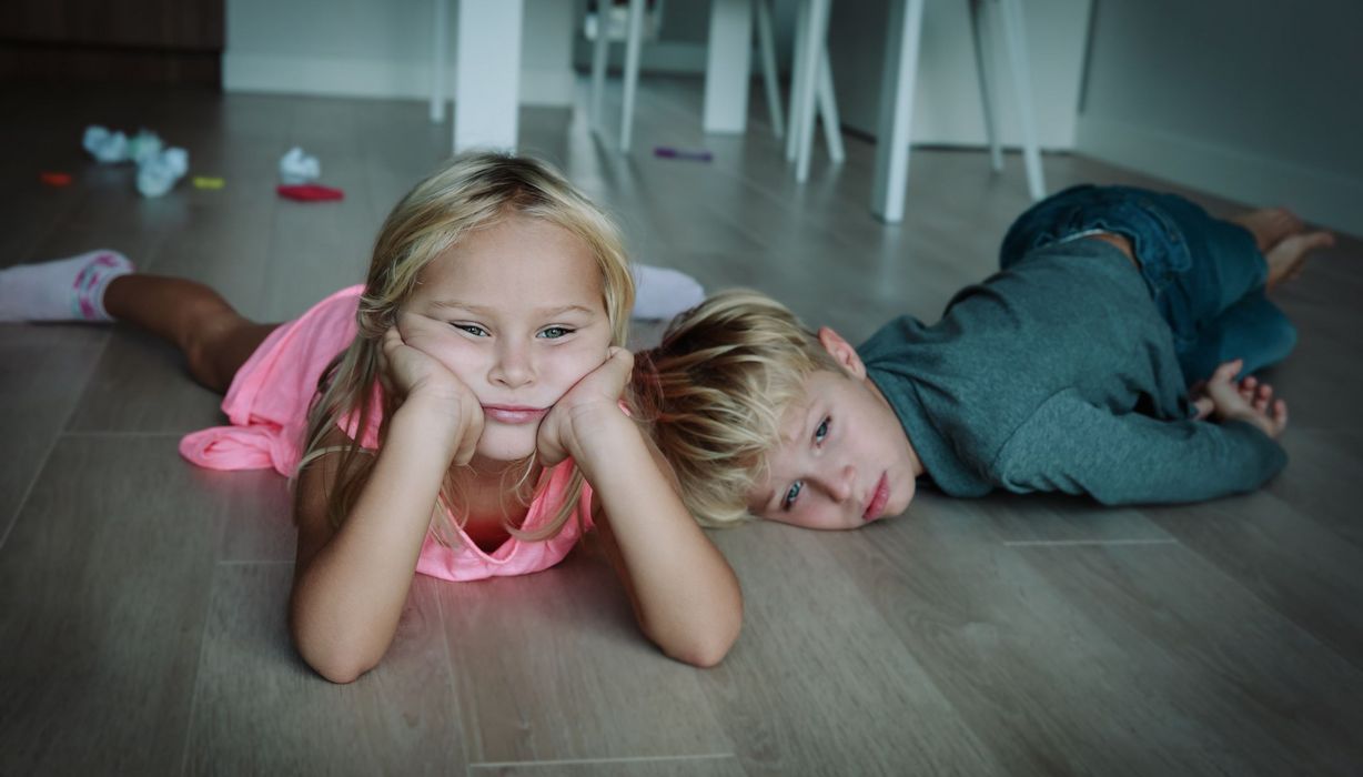 Zwei Kinder, liegen gelangweilt und deprimiert auf dem Boden.