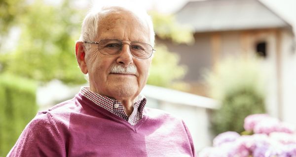 Älterer Mann mit Brille und violettem Pulli blickt in die Kamera.