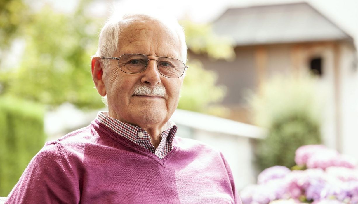 Älterer Mann mit Brille und violettem Pulli blickt in die Kamera.