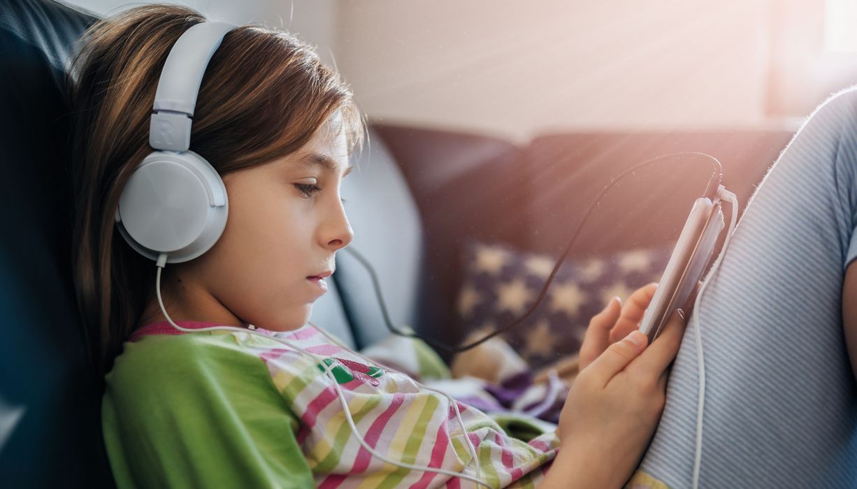 Mädchen sitzt mit Tablet und Kopfhörern auf dem Sofa 