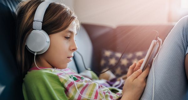 Mädchen sitzt mit Tablet und Kopfhörern auf dem Sofa 