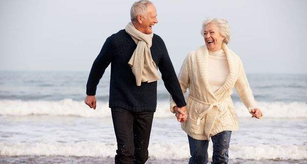 Senioren-Paar, laufend lachend am Strand entlang.