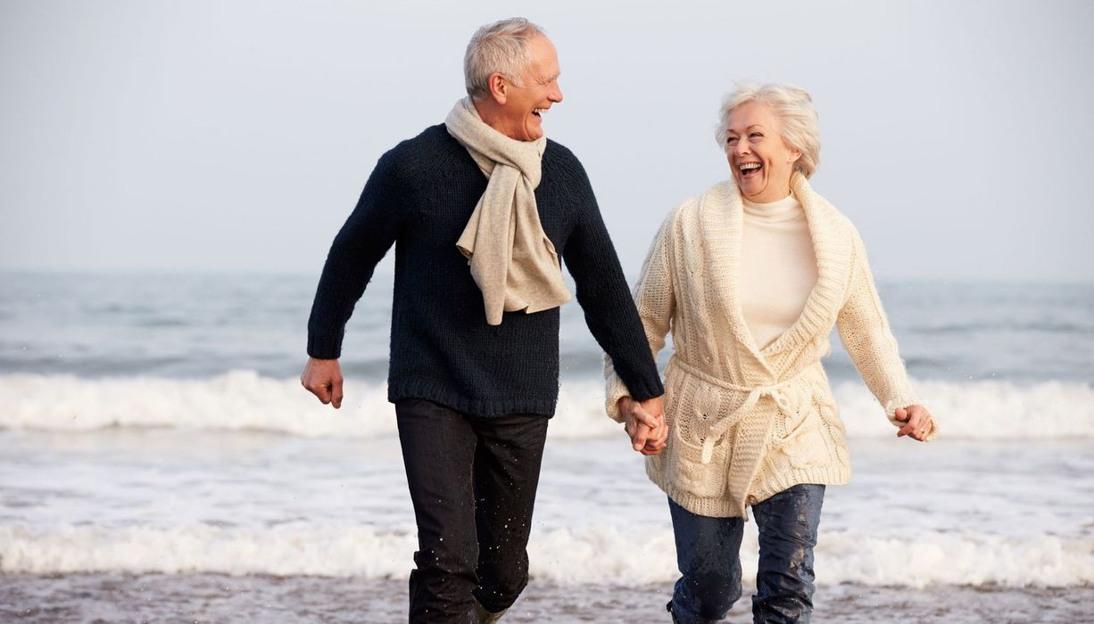 Senioren-Paar, laufend lachend am Strand entlang.