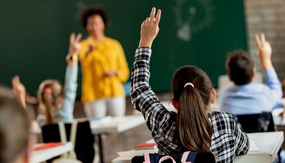 Mädchen, sitzt in einem KLassenzimmer und meldet sich.