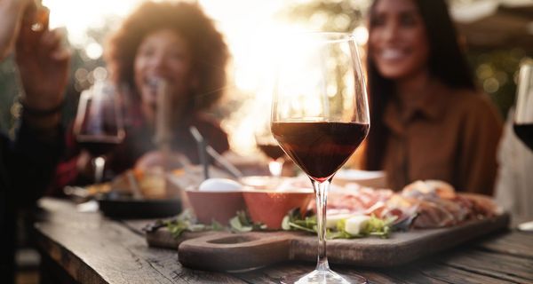 Glas Rotwein, im Hintergrund zwei Freundinnen und Essen.