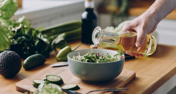 Mann, gießt Öl auf einen Salat.