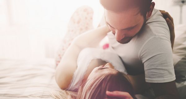 Junge Frau und Mann bekleidet im Bett, er beugt sich über sie.