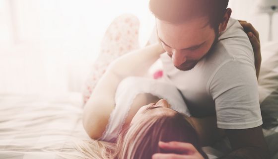 Junge Frau und Mann bekleidet im Bett, er beugt sich über sie.