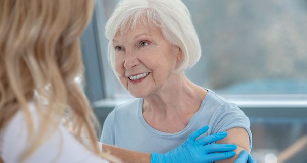 Krankenschwester klebt einer älteren Dame ein Pflaster auf den Link Oberarm - wohl nach einer Impfung.