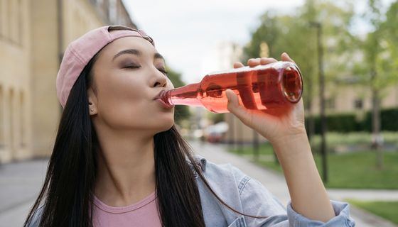 Frau trinkt hellrote, transparente Flüssigkeit aus einer Glasflasche.