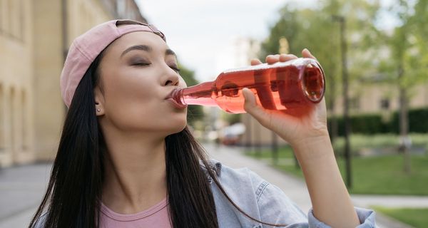 Frau trinkt hellrote, transparente Flüssigkeit aus einer Glasflasche.