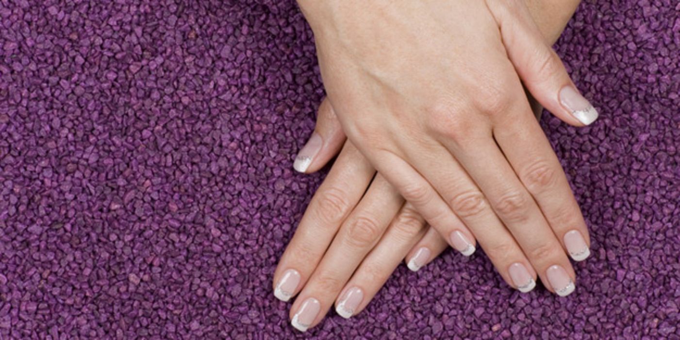 Zwei Frauenhände mit manikürten Fingernägeln vor lila Hintergrund.