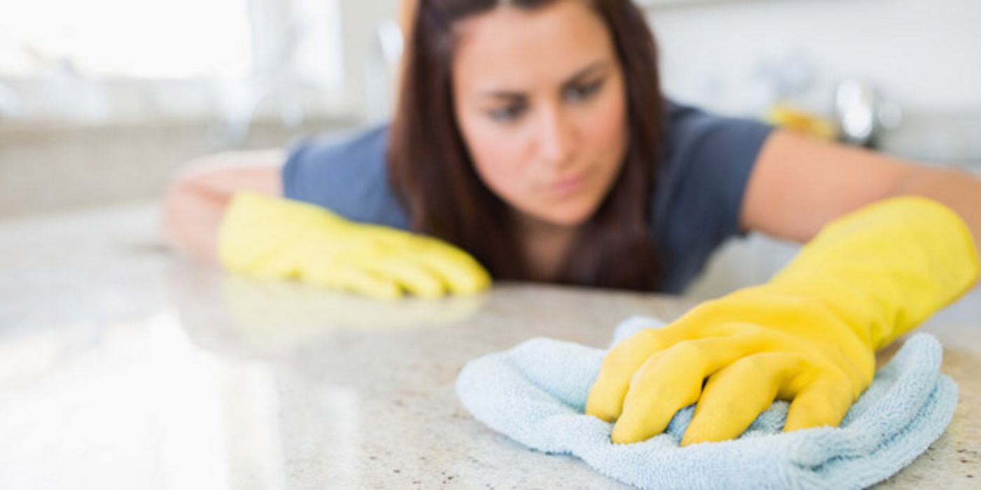 Frau mit gelben Gummihandschuhen putzt Küche.