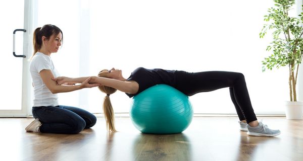 Schmerztherapeutin mit Patientin, macht Übungen mit einem Gymnastikball.