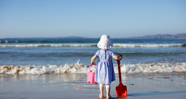 Kleines Mädchen, steht am Strand mit Sonnenhut. 