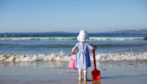 Kleines Mädchen, steht am Strand mit Sonnenhut. 
