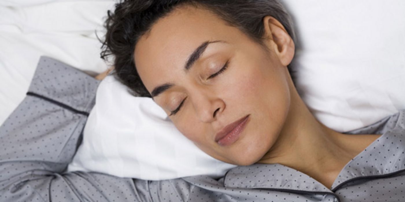 Junge Frau mit kurzen dunklen Haaren liegt im Bett und schläft.