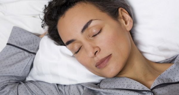 Junge Frau mit kurzen dunklen Haaren liegt im Bett und schläft.