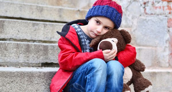 Kindergartenkind, ca. 5 Jahre alt, Mütze, Anorak, Jeans, einen Teddy im Arm, sitzt traurig auf einer grauen Steintreppe