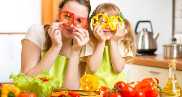 Mutter mit Kind, zusammen in der Küche, halten sich zwei Paprika-Scheiben vor die Augen.