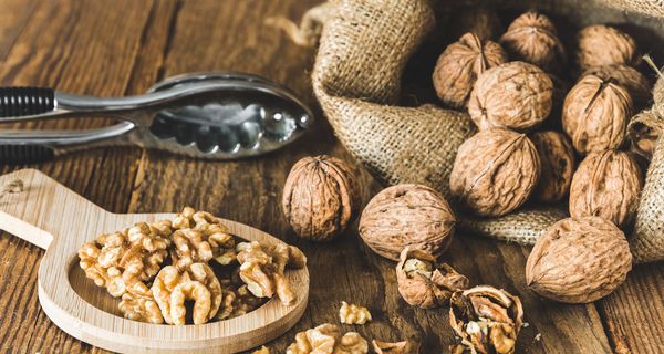 Walnüsse, ganz mit Schale, ein Nussknacker und geknackte Nüsse auf einem Holztisch.