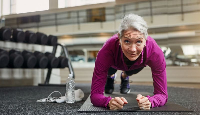 eine ältere Frau macht im Fitnessstudio eine Plank.