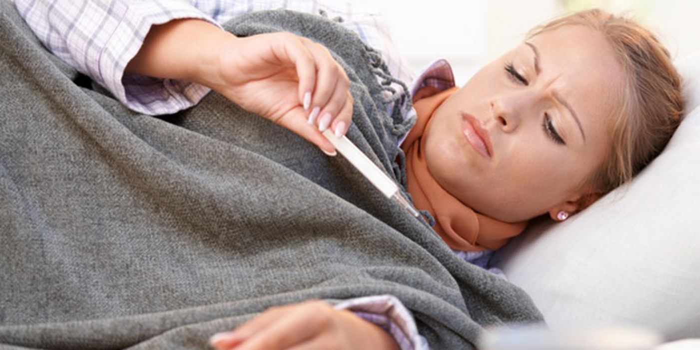 Kranke Frau liegt im Bett und liest die Anzeige eines Thermometers ab