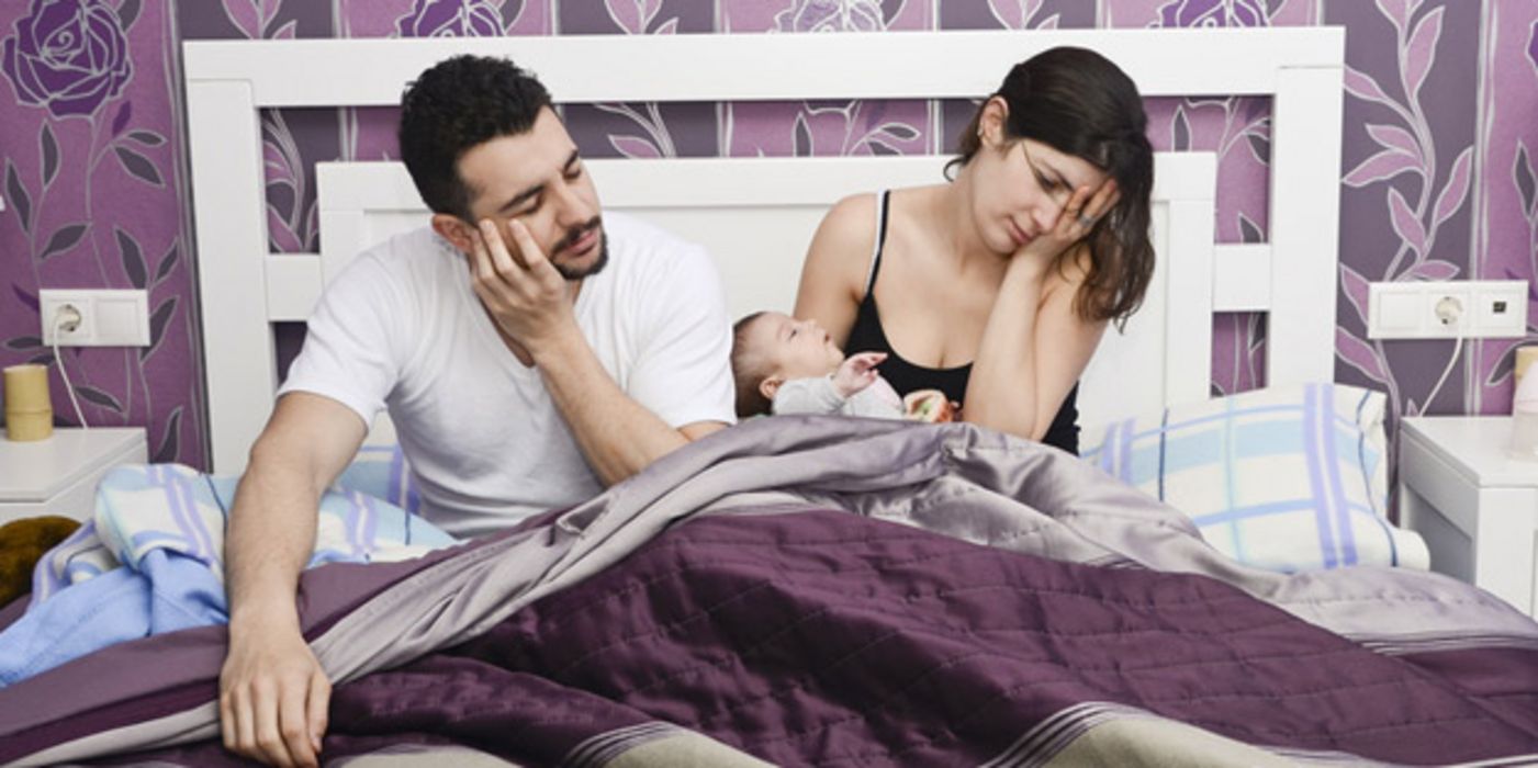 Schlafgestörtes Paar in den 20ern im Bett sitzend, Frau mit Säugling im Arm